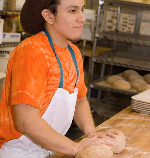 great harvest employee rolling out dough on a table